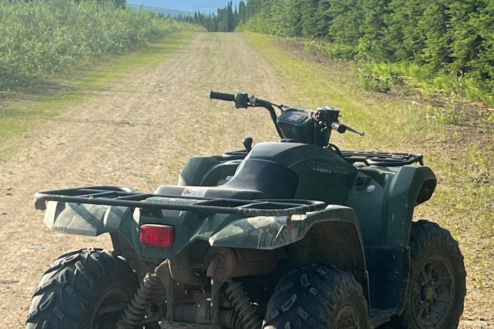 An ATV on a dirt road surrounded by trees and distant mountains.