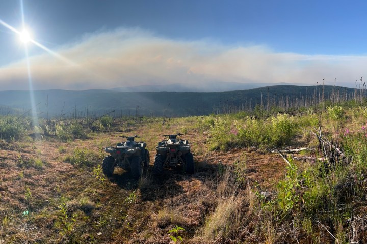 Hilly landscape with two ATVs under a bright sun and clear blue sky.