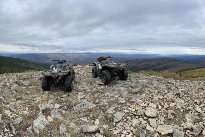 Two ATVs on a rocky hilltop overlooking a vast landscape under a cloudy sky.