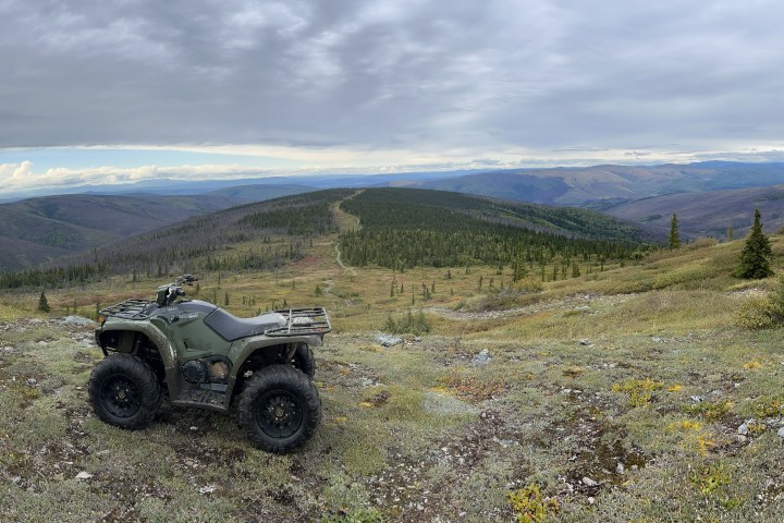 ATV on a rocky hill with expansive mountain views under a cloudy sky.