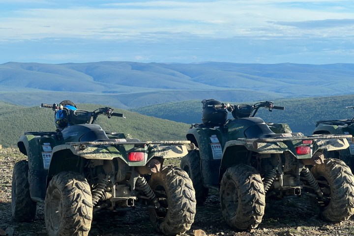 Three ATVs parked on a hill overlooking vast, rolling hills under a cloudy sky.
