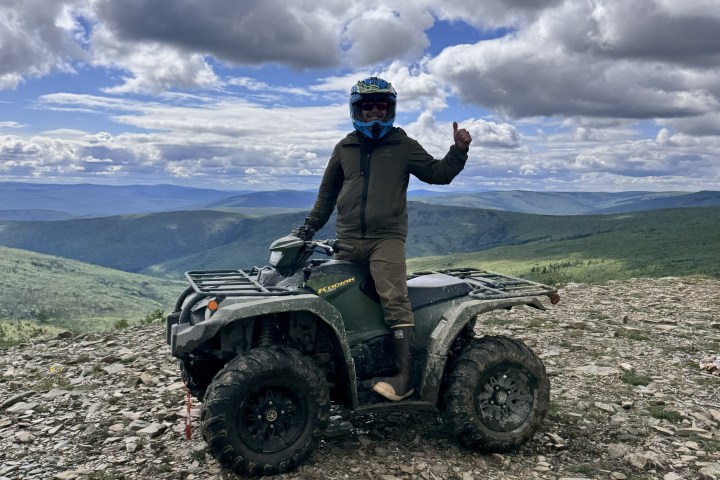 Person on an ATV atop a rocky hill with a scenic view and cloudy sky.