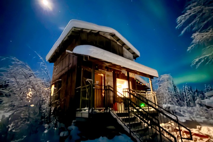 Snow-covered cabin under moonlit sky with aurora borealis.