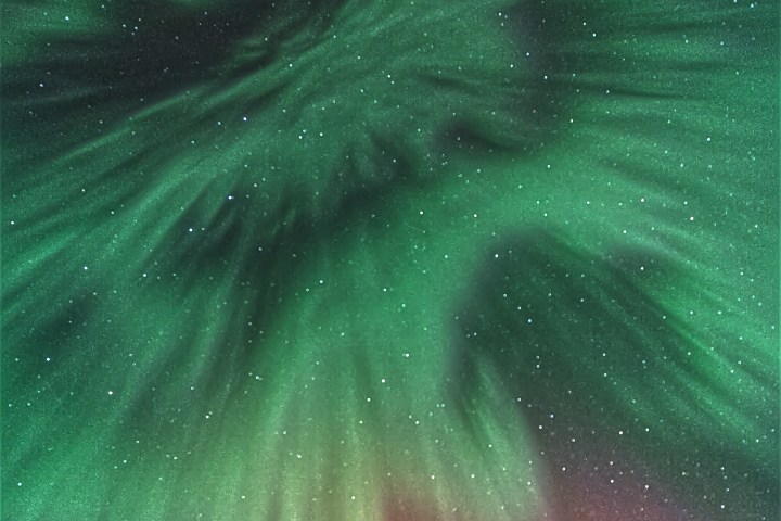 Green and purple aurora borealis display in starry night sky.